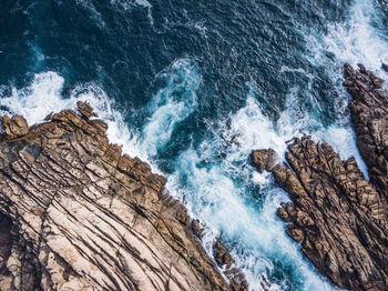 High angle view of waves splashing on rock formations at beach