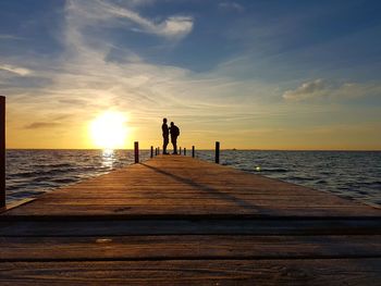 Silhouette men standing on pier over sea against sky during sunset