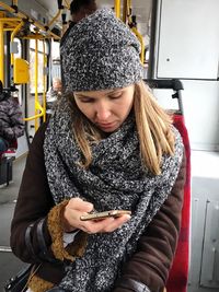 Woman wearing knit hat using smart phone while sitting in bus