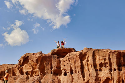 Low angle view of man standing on rock against sky