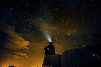 Rear view of man with flashlight against sky at night