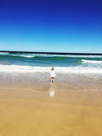 Rear view of girl standing at beach against clear blue sky