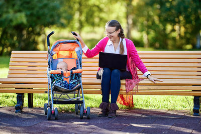 Side view of woman using mobile phone while sitting on bench in park