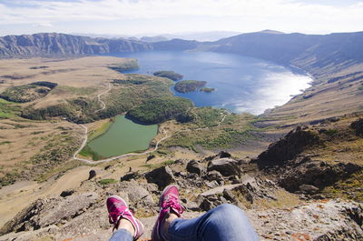 Low section of woman sitting on cliff against lake