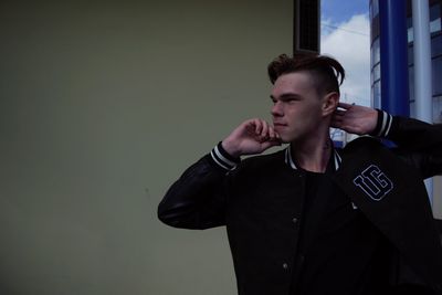 Young man looking away while standing against wall