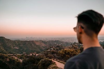Rear view of man looking at cityscape against sky during sunset