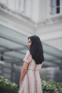 Low angle view of woman looking away while standing against built structure