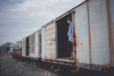 Man standing in abandoned freight train against sky