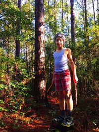 Portrait of boy standing by tree in forest