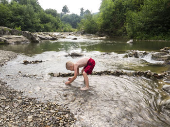 Side view of shirtless boy playing in river