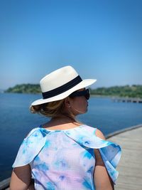 Rear view of woman wearing hat looking away while standing against sea