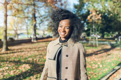 Beautiful african american young woman with afro hairstyle in a stylish coat in a park, smiling