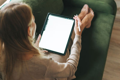 Beautiful blonde young woman artist illustrator drawing on tablet with white screen at home, mockup