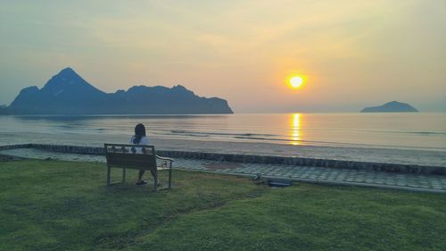 Rear view of people sitting on bench at sunset