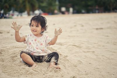 Portrait of cute girl sitting on sand at beach