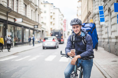 Portrait of confident food delivery man with bicycle on street in city