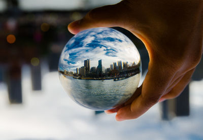 Cropped hand holding crystal ball with reflecting of modern buildings against sky