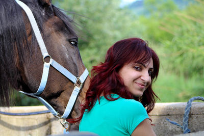 Portrait of young woman standing by horse against trees