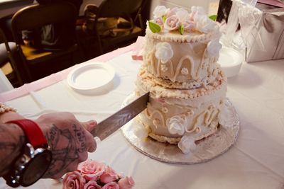 Cropped hands of couple cutting wedding cake