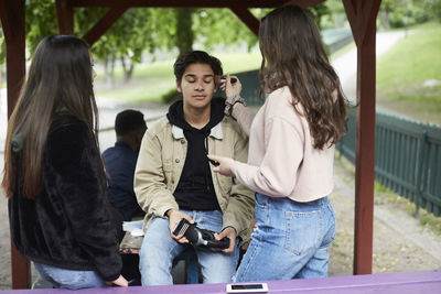 Female looking teenage girl applying make-up on male friend