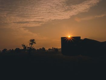 Silhouette trees on field against orange sky