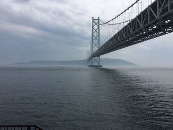 Low angle view of akashi strait bridge over river against cloudy sky