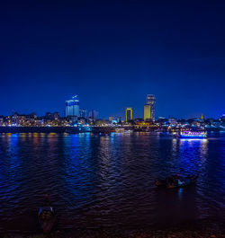 Illuminated buildings by river against sky at night