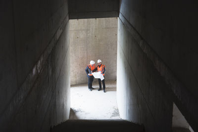 Two men with plan wearing safety vests talking in building under construction