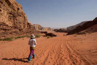 Rear view of woman walking at desert against clear sky