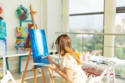 Rear view of young woman painting at home