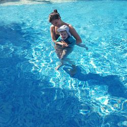 High angle view of happy mother carrying baby in swimming pool