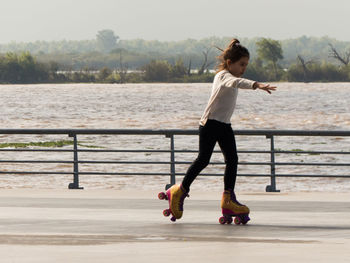 Girl roller skating on footpath against lake