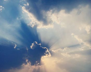 Low angle view of sunlight streaming through clouds