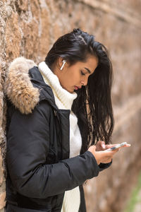 Beautiful brunette young woman in winter clothes using smartphone listening to music with earphones