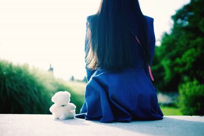 Rear view of girl sitting by toy on retaining wall