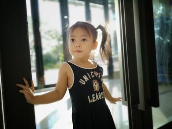 Girl looking away while standing against window