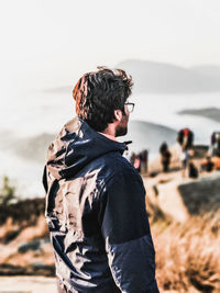 Side view of young man standing by sea against sky