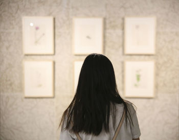 Rear view of woman standing against wall at home