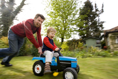 Father and son riding toy car in backyard