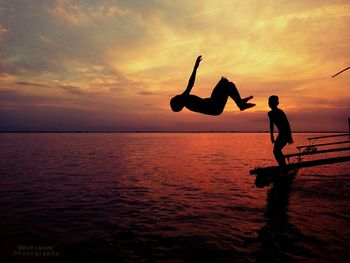 Boys jumping into water at sunset