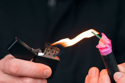 Close-up of person holding lit candle against black background