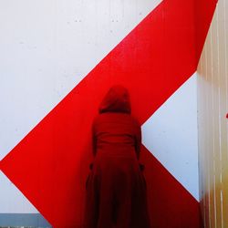Rear view of person standing against red wall