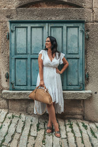 Full length portrait of beautiful young woman standing in front of blue window shutters in old town