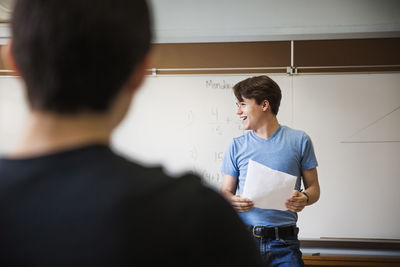 Man holding paper while standing against whiteboard in classroom