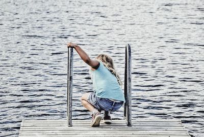 Rear view of man sitting on wood against lake