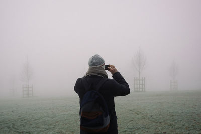 Rear view of man using mobile phone in foggy weather