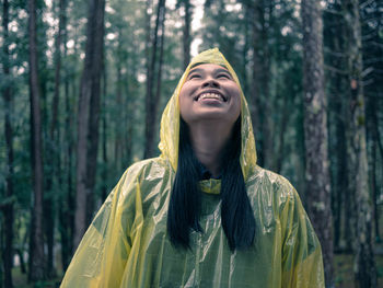 Smiling woman wearing raincoat in forest