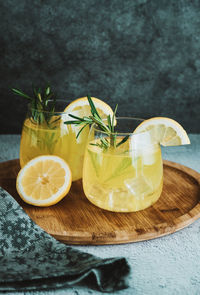 Glasses with cold cocktail, lemonade, sliced lemon and rosemary plant on the concrete table