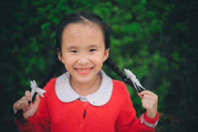 Close-up portrait of cheerful girl with pigtails against plants