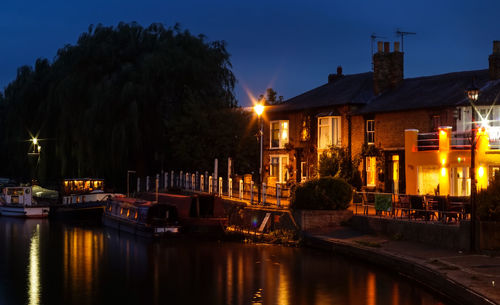 Illuminated buildings by river against sky at night